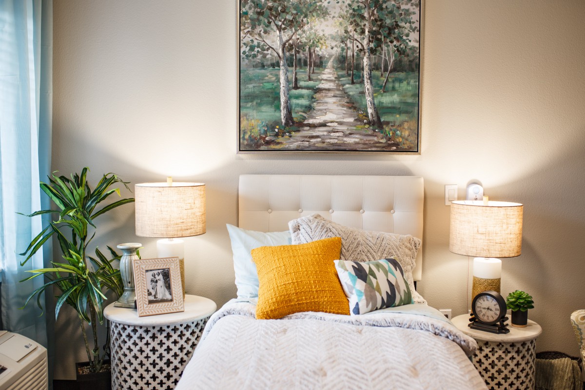 A cozy and modern bedroom with a large artwork above the bed, flanked by stylish lamps and decorative pillows.