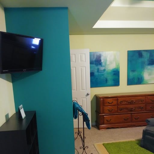 A cozy living room with a wall-mounted TV, colorful artwork, and wooden furniture.
