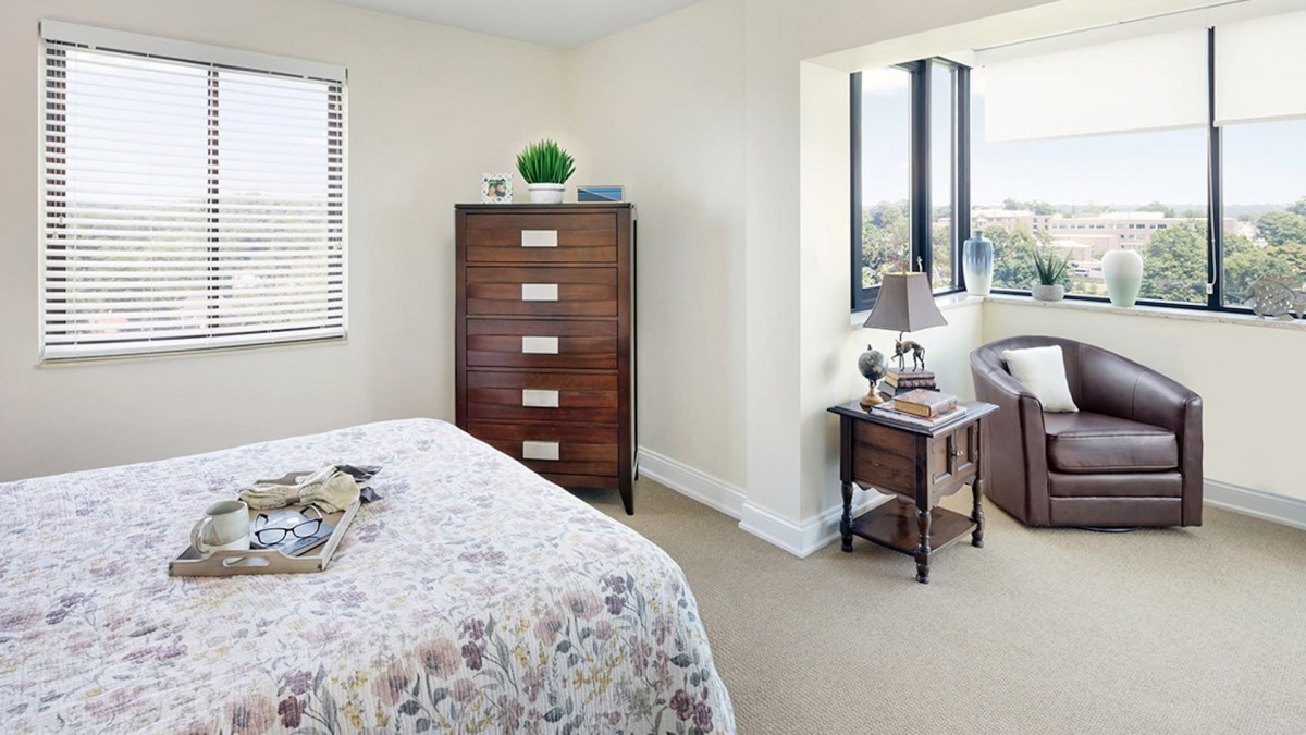 A cozy bedroom with a chest of drawers and a bedside table near a window.