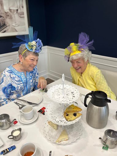 Two elderly women enjoying a delightful tea party with scones and wearing colorful hats.