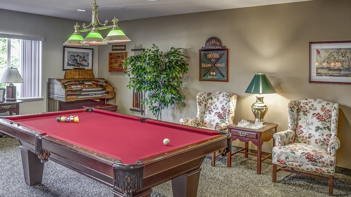 A cozy game room featuring a red felt pool table, elegant decor, and comfortable seating.