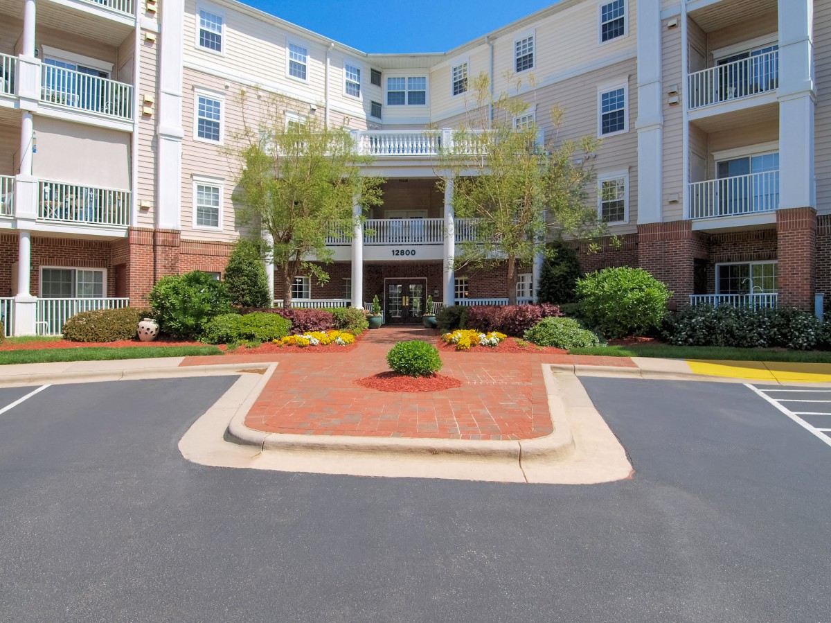 A view of a multi-story apartment building with well-maintained landscaping at the entrance.