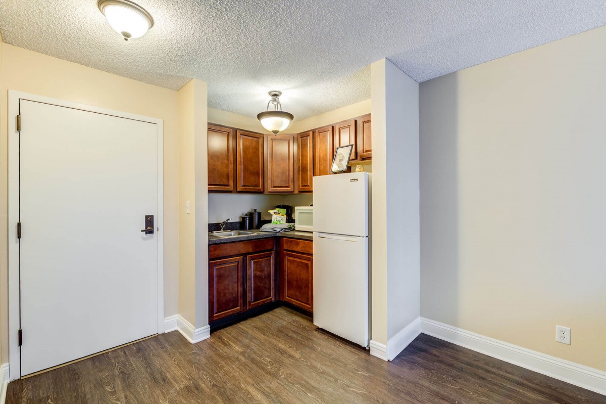 A compact apartment kitchen featuring wooden cabinets and a white refrigerator.