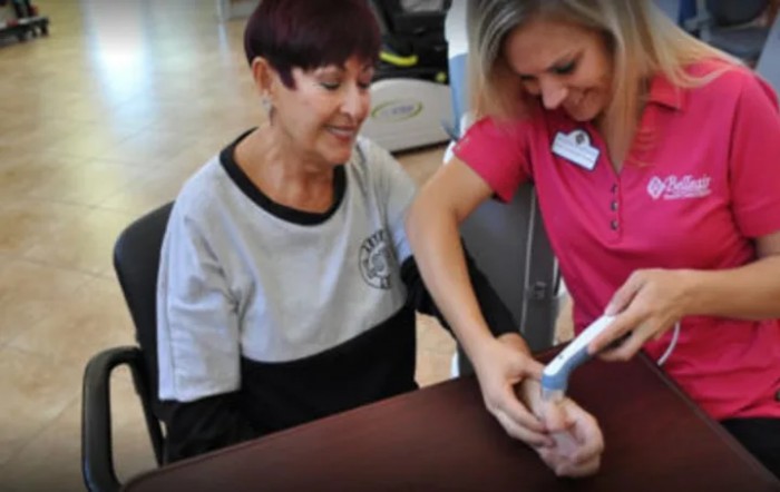 A healthcare professional assists an elderly woman with a physical therapy device.