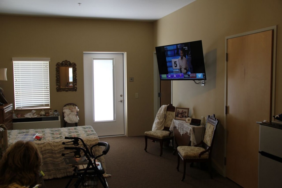 A cozy living room with a wall-mounted television, two chairs, and a small table near the door.