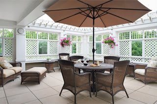 A cozy patio with a round table and chairs under an umbrella, surrounded by lattice fencing and potted plants.