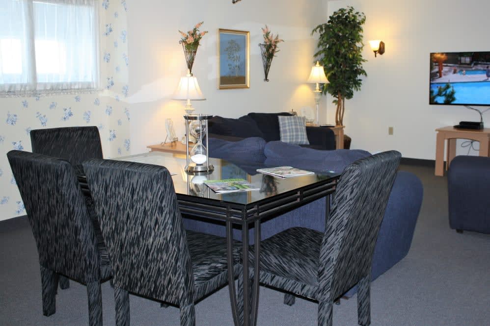 A cozy living and dining area featuring a glass-topped table, patterned chairs, decorative wall art, and ambient lighting.