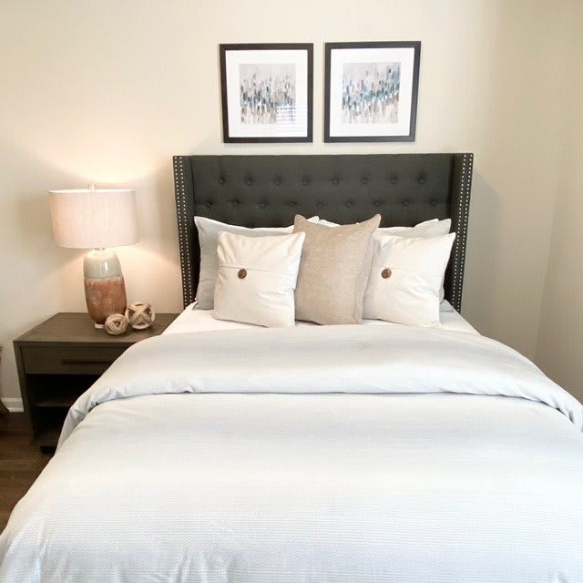 A neatly arranged bedroom with a modern headboard, decorative pillows, and framed artwork above the bed.