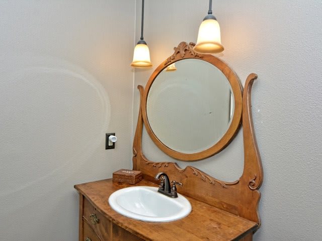 A bathroom vanity with an ornate wooden mirror and a sink, flanked by two pendant lights.