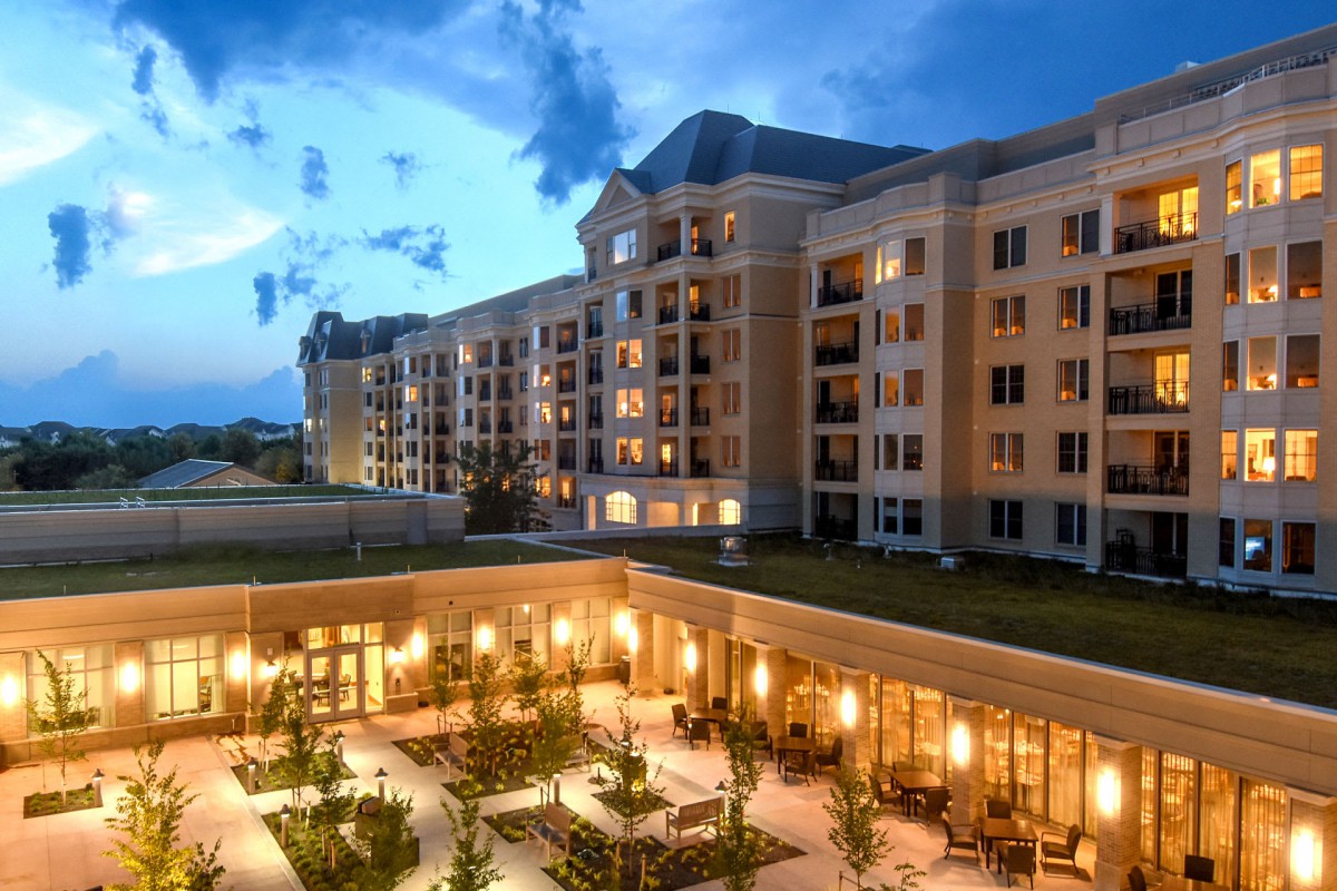 A well-lit residential building with a courtyard in the evening under a cloudy sky.