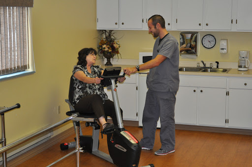 A healthcare professional assists a patient during a physical therapy session on an exercise bike.
