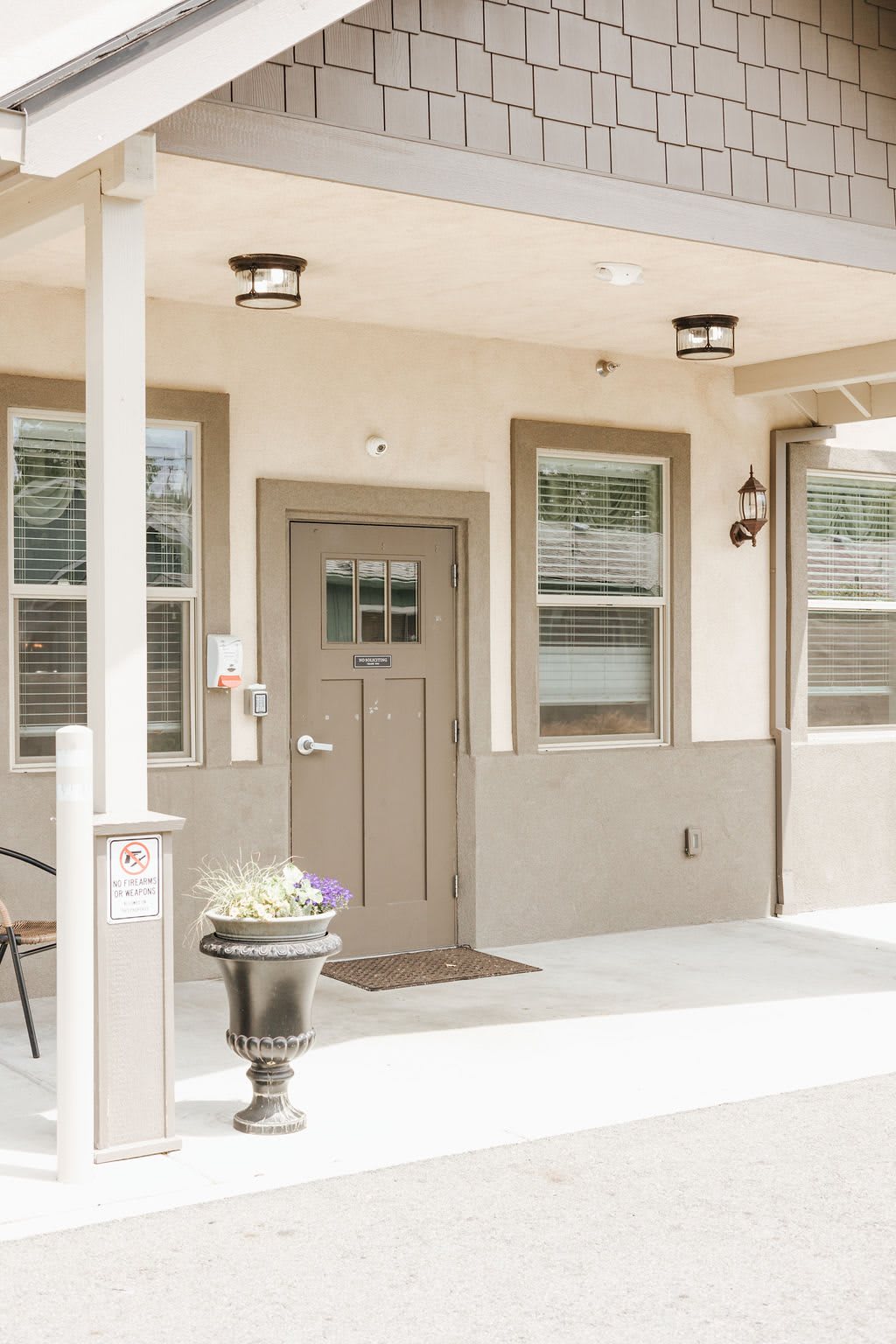 A well-maintained building exterior featuring a main door, windows with blinds, outdoor lighting fixtures, and a decorative planter on the porch.