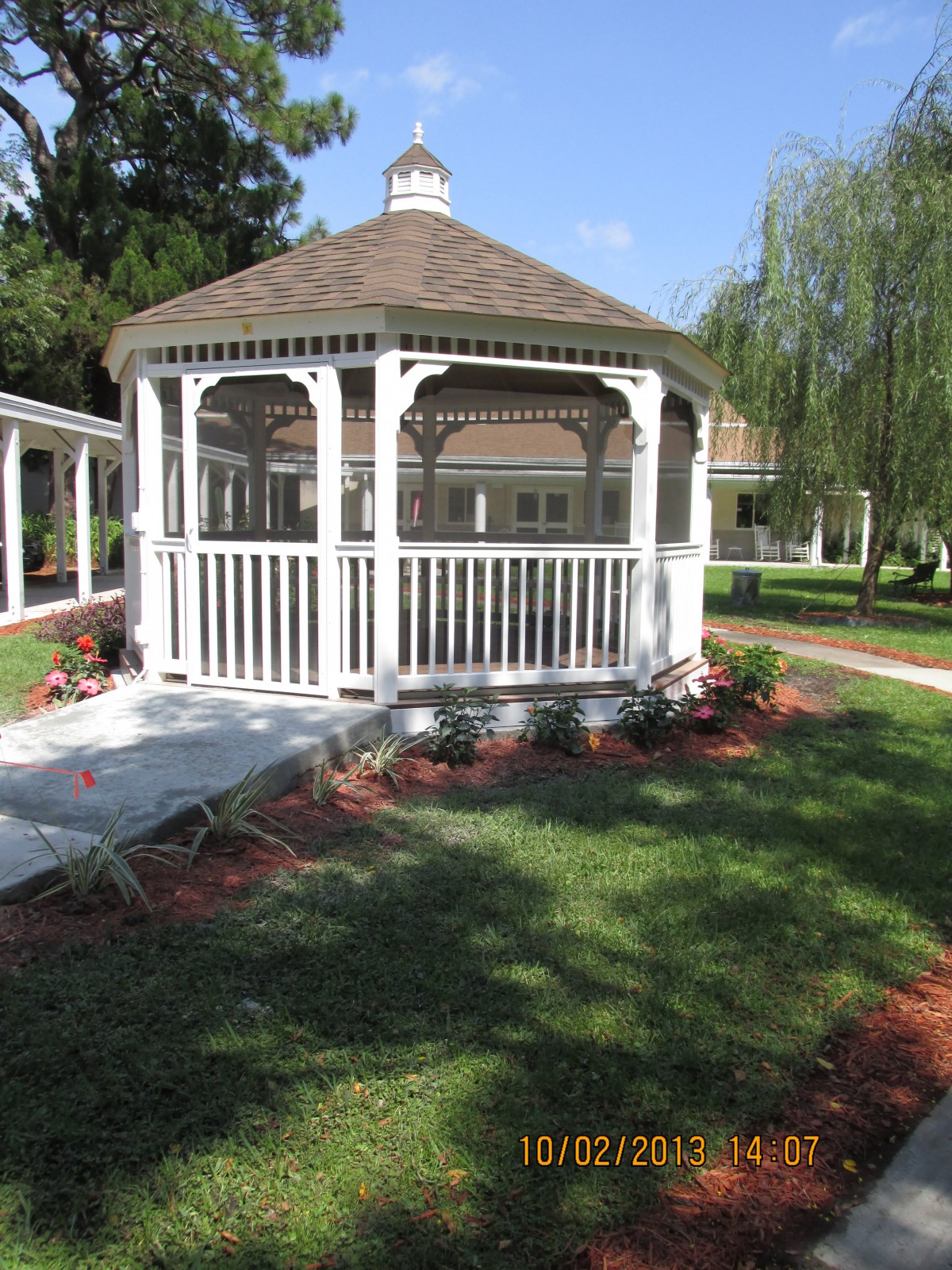 A charming white gazebo in a landscaped garden setting.