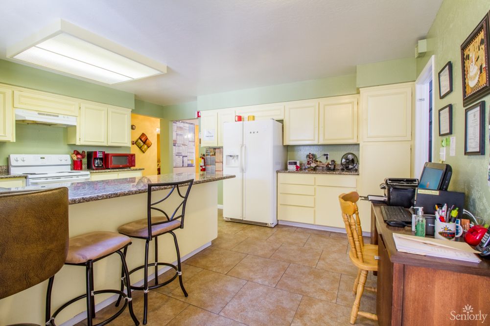 A spacious kitchen with cream-colored cabinets, bar stools at the counter, and various appliances.