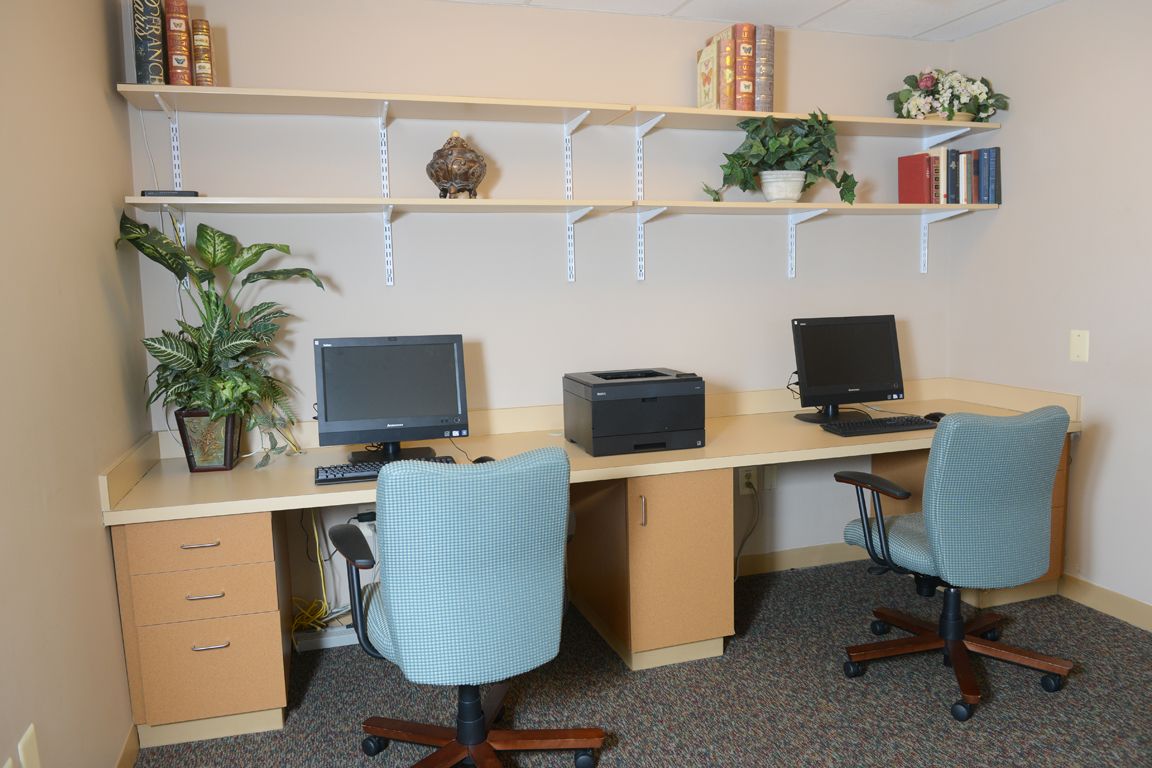 A tidy office workspace with computers, a printer, and decorative plants.