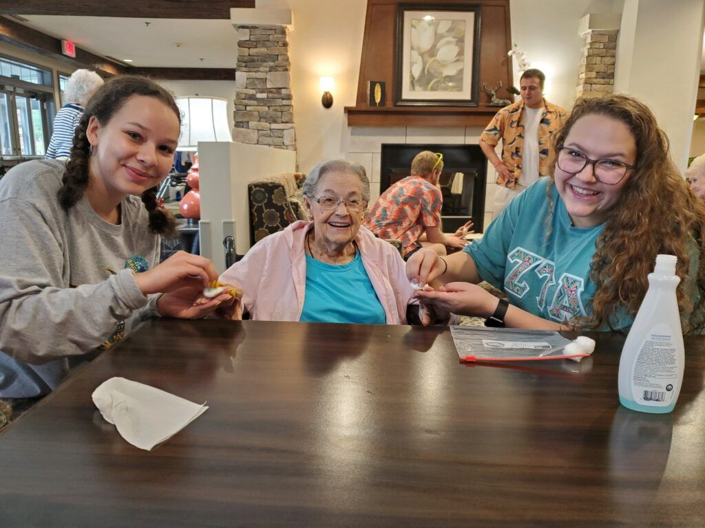 Two young women spending time with an elderly woman at a table indoors.