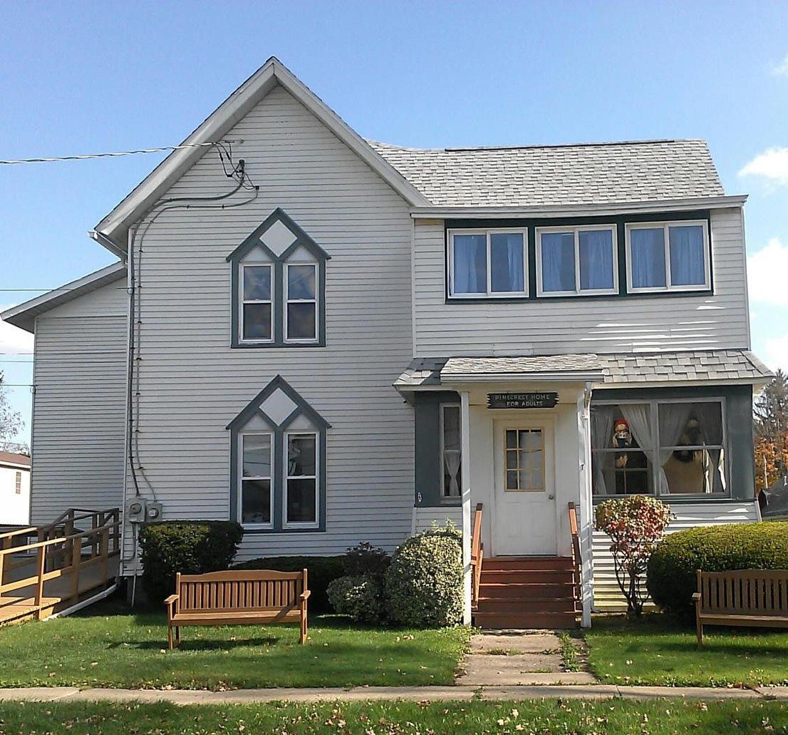 A residential house with a gabled roof and multiple windows in a grassy yard.