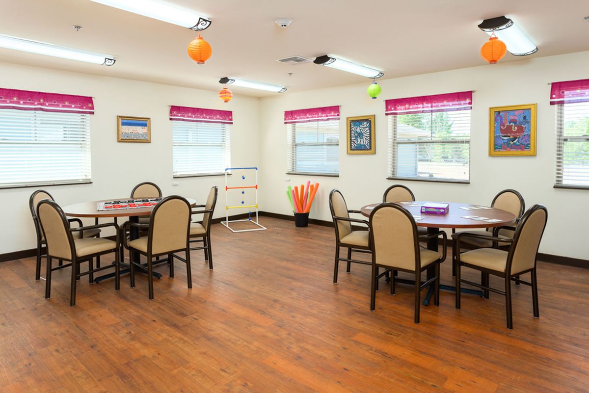 A well-lit dining area with several tables and chairs, featuring bright decor and wooden flooring.