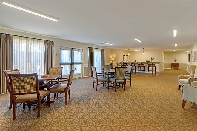 Spacious dining area with tables and chairs, featuring carpet and natural lighting.