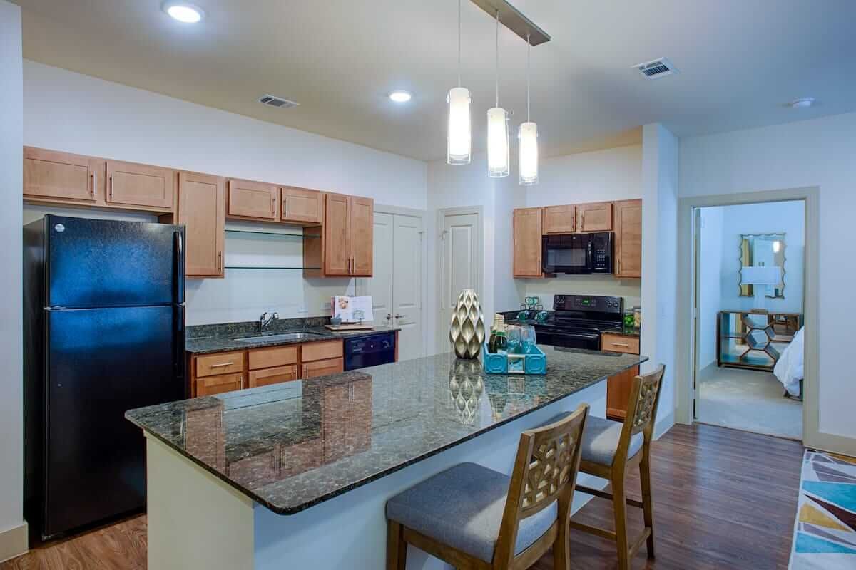 A modern kitchen with an island, bar stools, and stainless steel appliances.