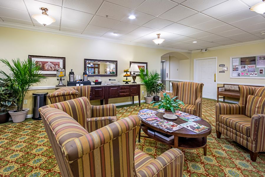 A cozy lobby seating area with striped armchairs, a central coffee table, decorative plants, and artwork on the walls.
