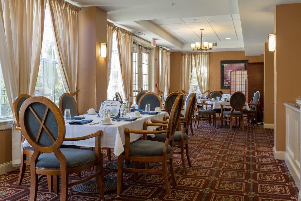 An elegant restaurant dining room with neatly arranged tables and chairs, adorned with soft curtains and warm lighting.