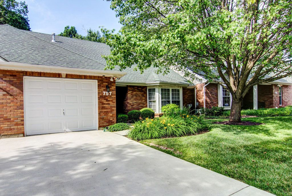 A charming brick house with a well-maintained front yard featuring a tree and greenery, alongside a driveway leading to an attached garage.