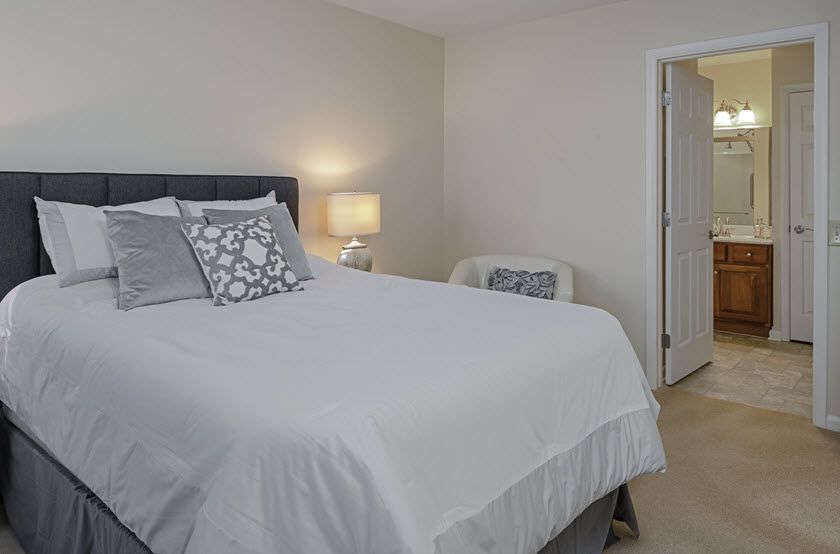 A cozy bedroom with a neatly made bed, decorative pillows, and a lamp on the nightstand.