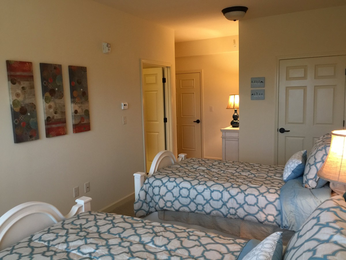 A cozy bedroom with twin beds, featuring modern patterned bedding and a warm lamp on a nightstand.
