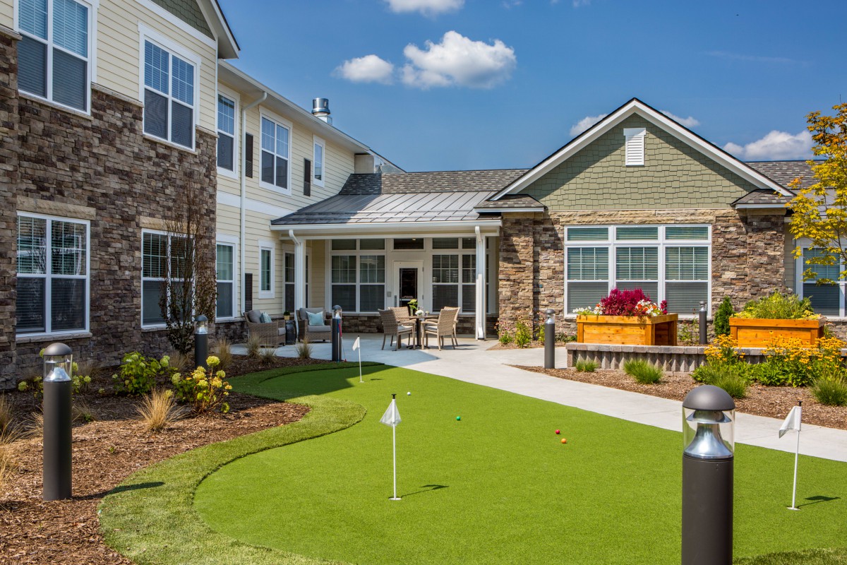 A residential building with a landscaped outdoor area featuring a putting green under a clear blue sky.