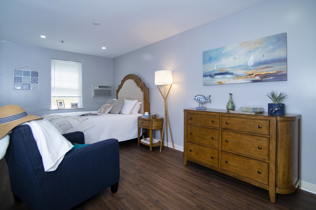A modern and cozy bedroom with a wooden floor, featuring a bed, dresser, and a stylish standing lamp.