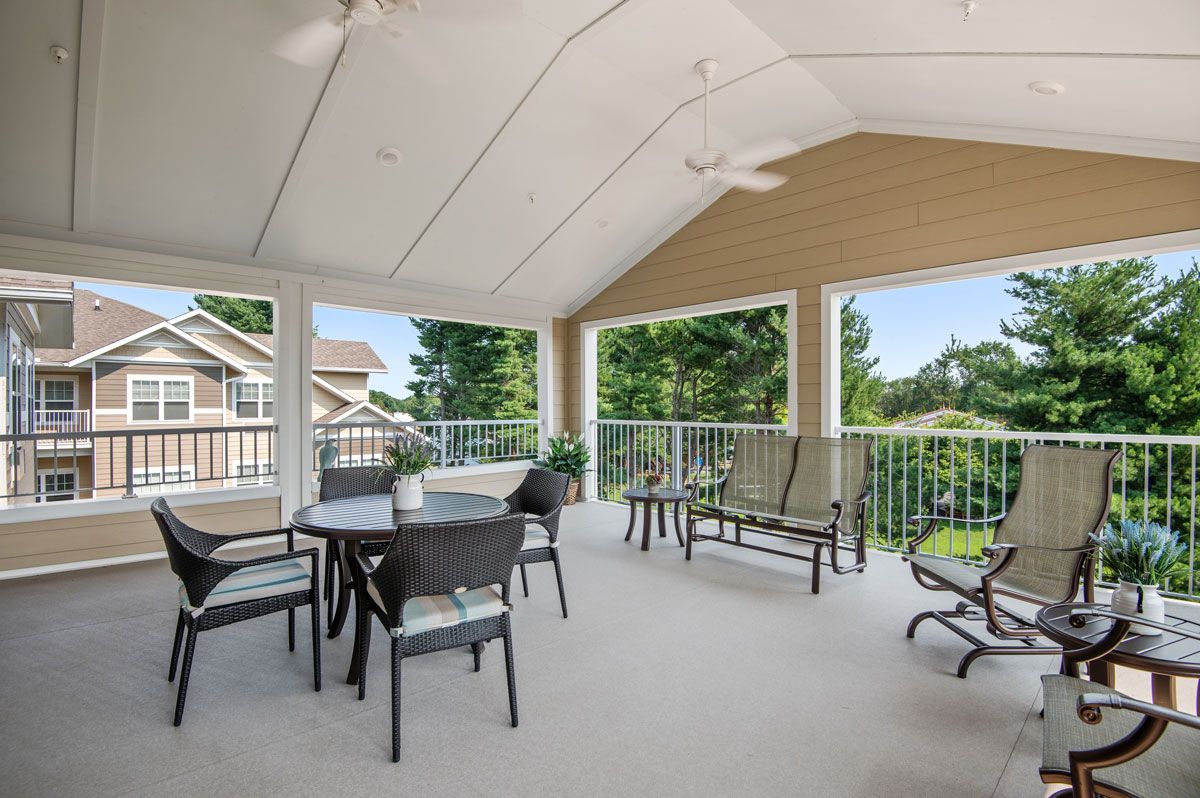 A spacious covered patio with outdoor furniture and ceiling fans, offering a view of greenery.