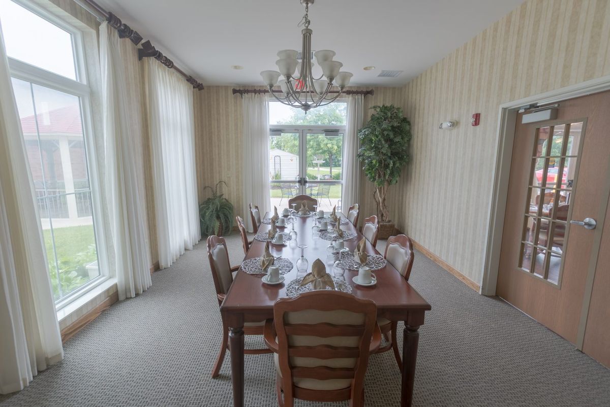 An elegantly set dining room with a long table, chandelier, and large windows allowing natural light.