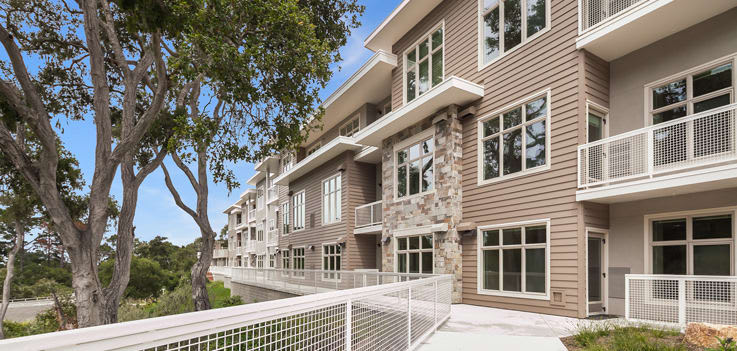 A modern apartment building with large windows and balconies, surrounded by trees.