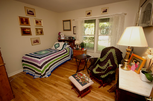 A cozy bedroom featuring a single bed with a striped blanket, a comfortable chair, and natural light streaming through the window.