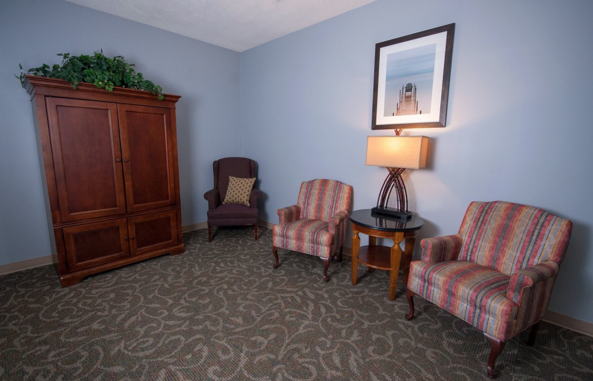 A cozy living room area featuring two striped armchairs, a side table with a lamp, and a wooden cabinet.