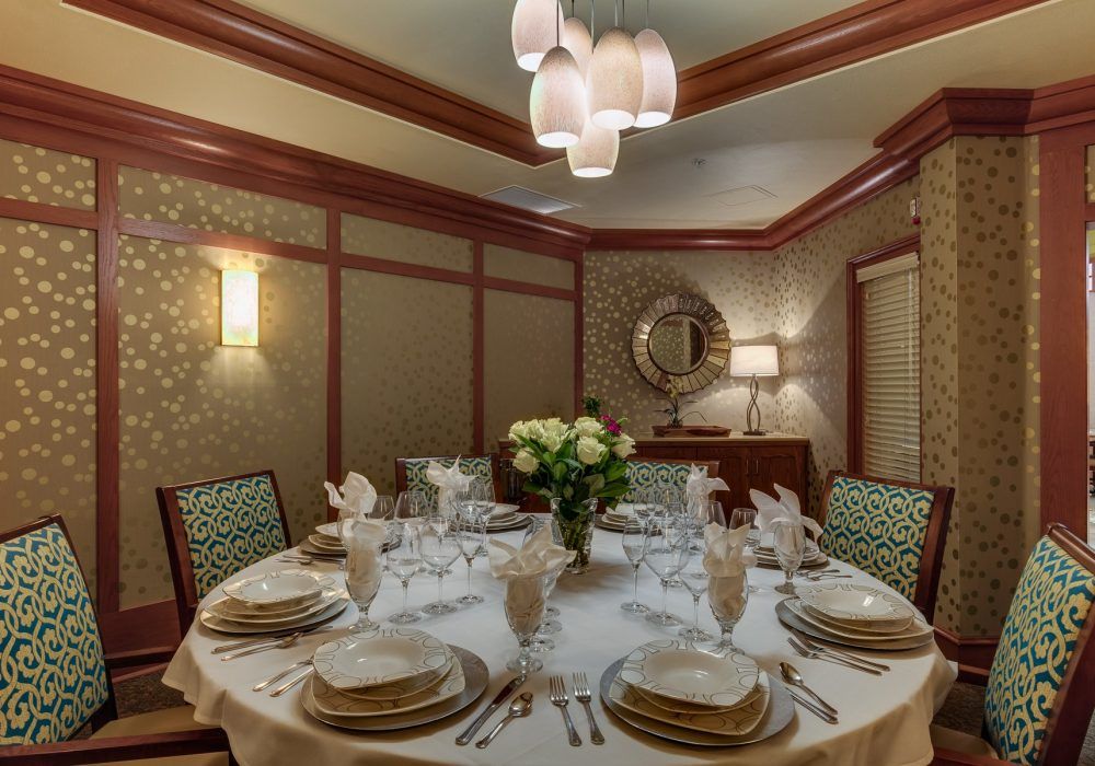A beautifully set dining table in an elegant room with a chandelier and floral centerpiece.