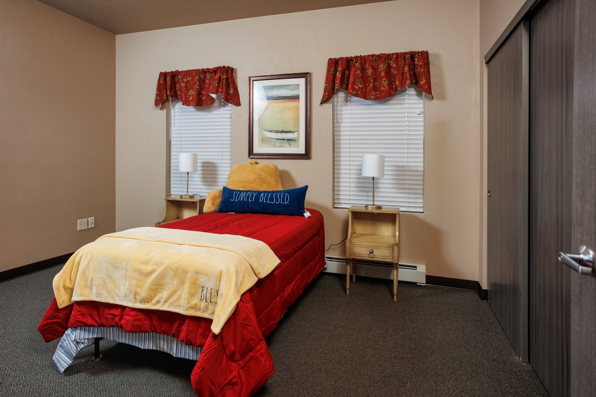 A cozy bedroom with a single bed, nightstands, and decorative lamps next to two windows.