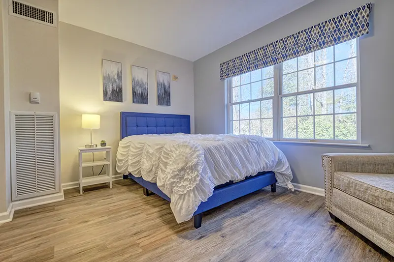 A bright bedroom with a blue headboard and large windows allowing natural light in.