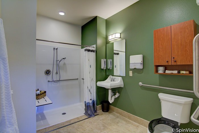 A modern, accessible bathroom with a shower, sink, and toilet featuring green walls and safety grab bars.