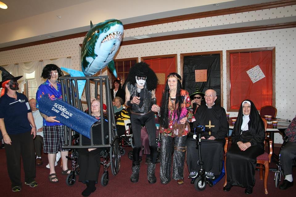 A group of people dressed in various costumes, including a person with a shark balloon, posing for a fun group photo at a party.