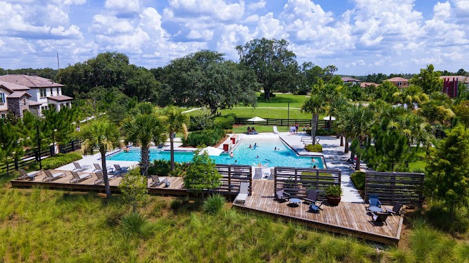 A serene outdoor pool area surrounded by lush greenery and a wooden deck, under a partly cloudy sky.