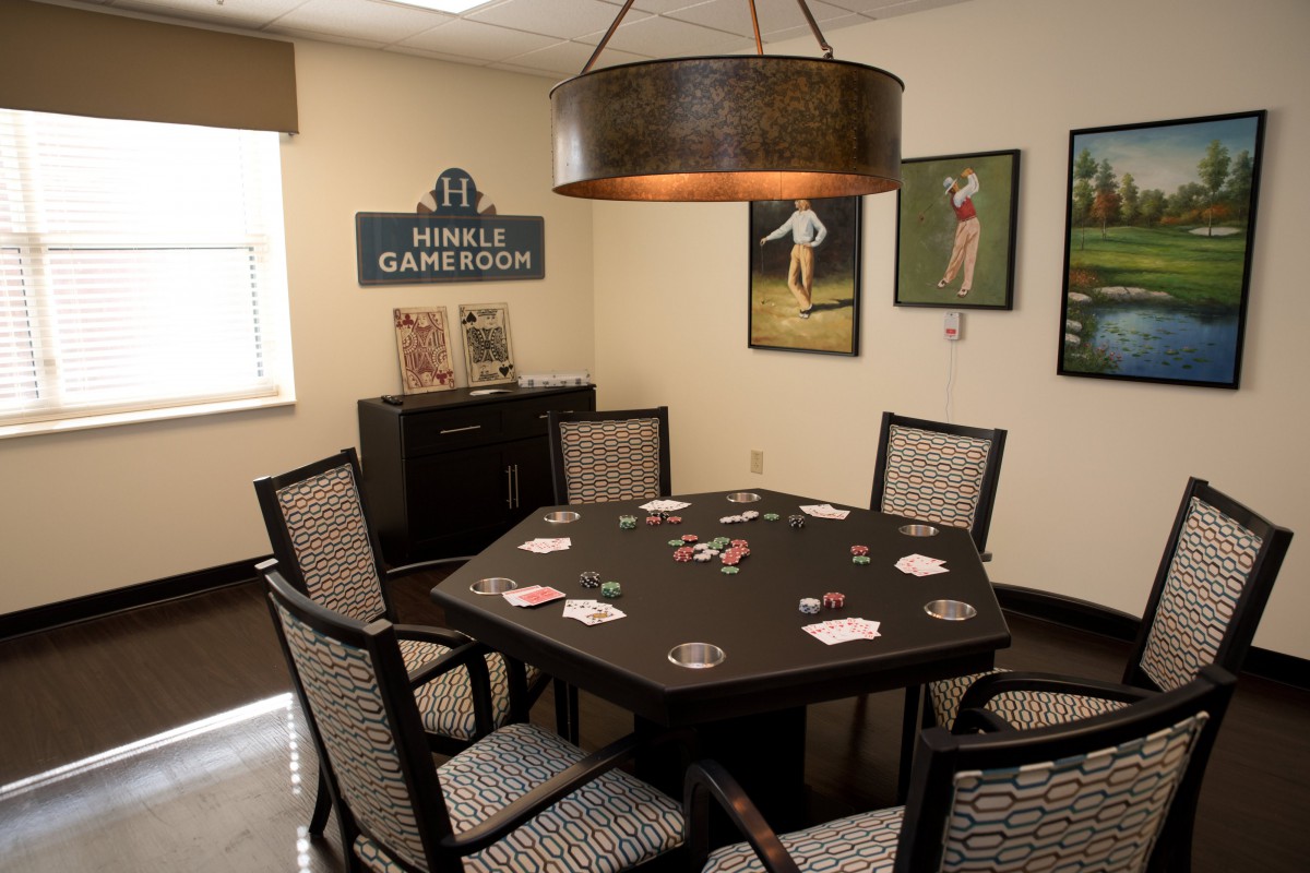 A cozy game room featuring a poker table surrounded by chairs, with sports-themed wall decor and ambient lighting.