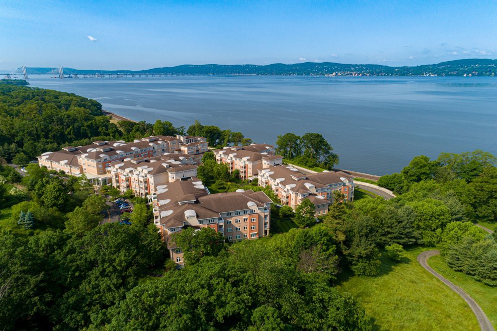 Aerial view of a residential complex by the river, surrounded by lush greenery.