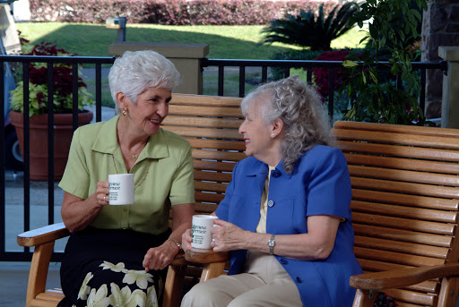 Two elderly women enjoying a cheerful conversation over coffee in a serene outdoor setting.