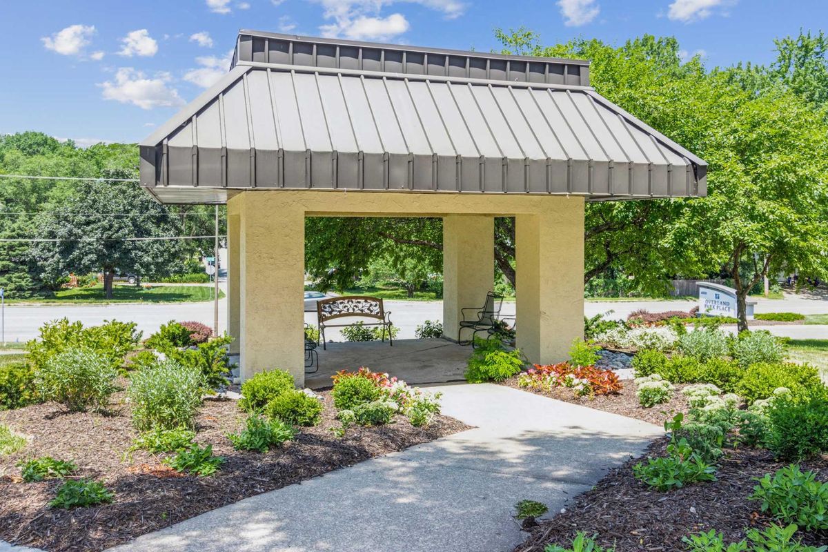 A charming gazebo surrounded by a lush garden with blooming flowers and a paved pathway.