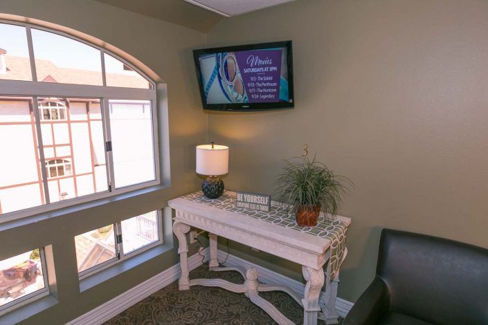 A cozy corner of a living room featuring a mounted television, decorative table with a lamp and plant, and an arched window.