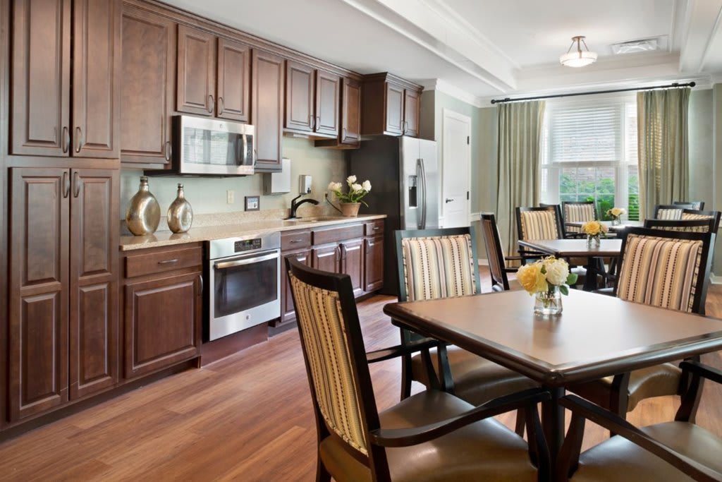 A modern kitchen and dining area featuring wooden cabinets, stainless steel appliances, and a hardwood floor.