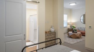 A cozy bedroom with an attached bathroom, featuring modern furniture and soft lighting.