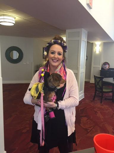 A cheerful woman poses with her dog in a cozy lobby setting.